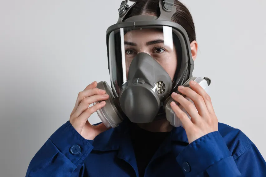 Safety worker inspecting and adjusting respirator mask for correct workplace fit and seal