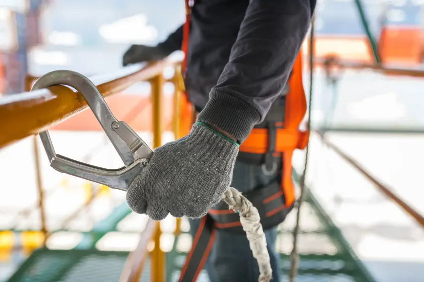 Construction worker safely connecting a harness while using hazard ID software to support workplace safety.