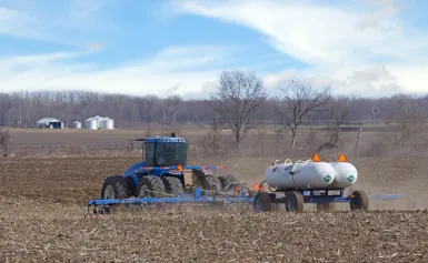 Farm tractor pulling twin NH₃ nurse tanks during field application, showing agricultural use of anhydrous ammonia.
