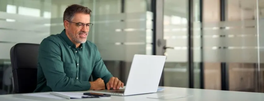 - BIS Safety Software Smiling busy older professional business man working on laptop sitting at desk while taking a virtual proctored online course