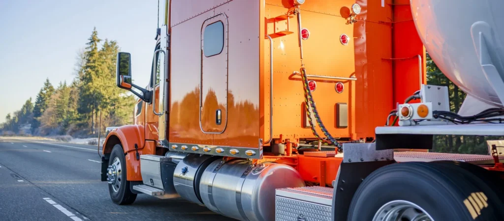 Pre Trip Inspection of Bright orange big rig semi truck transporting tank semi trailer