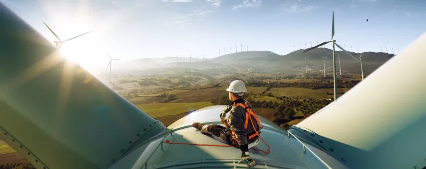 Happy engineer feel success after good work. He standing a top of windmill and looking beautiful sunset landscape