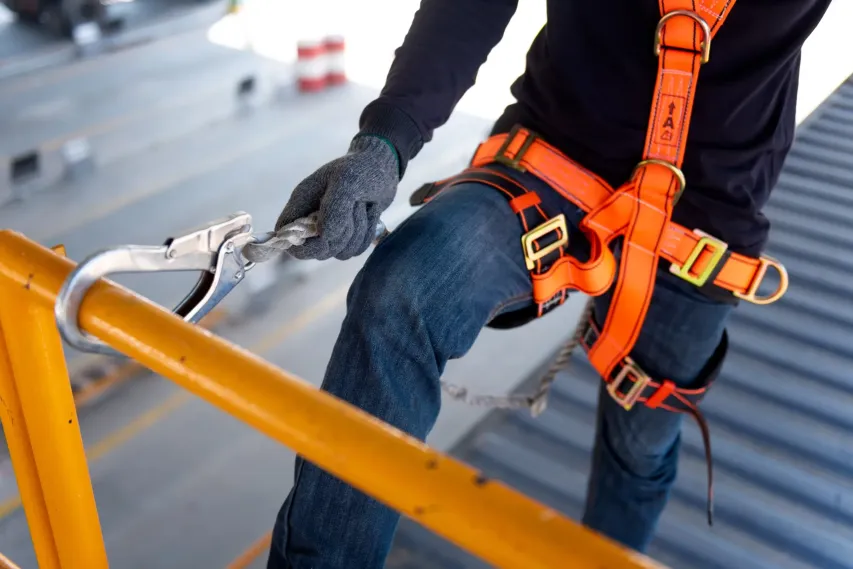 Canadian construction worker adjusting fall protection harness on job site