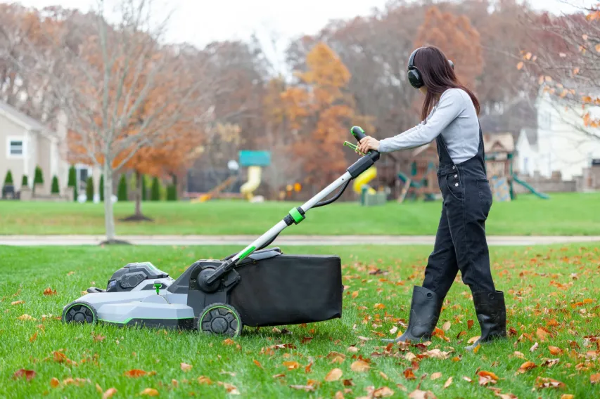 Worker pushing a walk-behind mower while wearing hearing protection in an outdoor setting.