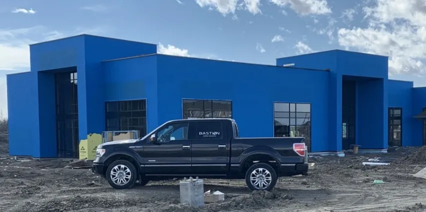 - BIS Safety Software Bastion safety truck on site. A large blue building lies behind a Bastion truck with a bastion insignia. A sunny blue sky with sparse cloud coverage frames the whole image.