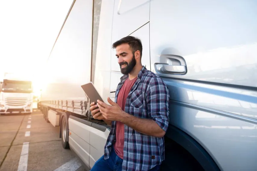 Man fills out truck pre trip inspection form digitally on his tablet while leaning on his truck on a sunny day.