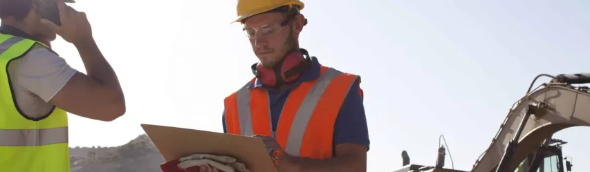 Two employees at a construction site, wearing orange and yellow work-jackets